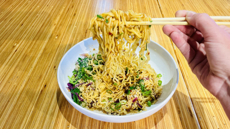 Hand with chopsticks grabbing ramen noodles from bowl