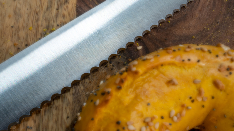 Close up of serrated knife with seeded bagel on a wooden cutting board