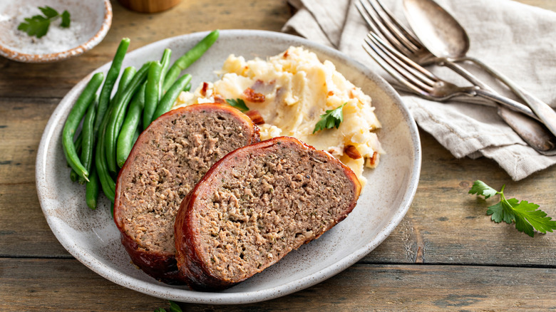 Meatloaf slices on a plate with mashed potatoes and green beans.